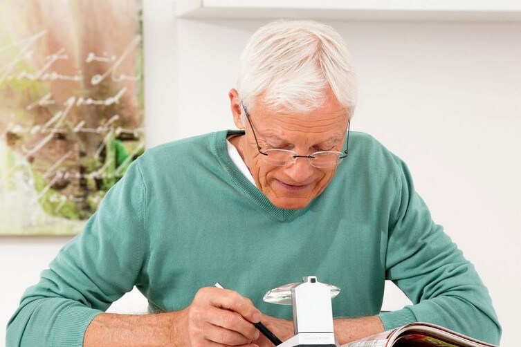 Senior mit Standleuchtlupe