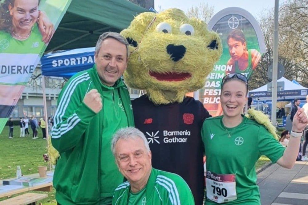  Rund um das Bayer-Kreuz 2026: Drei Läufer:innen mit einem Maskottchen