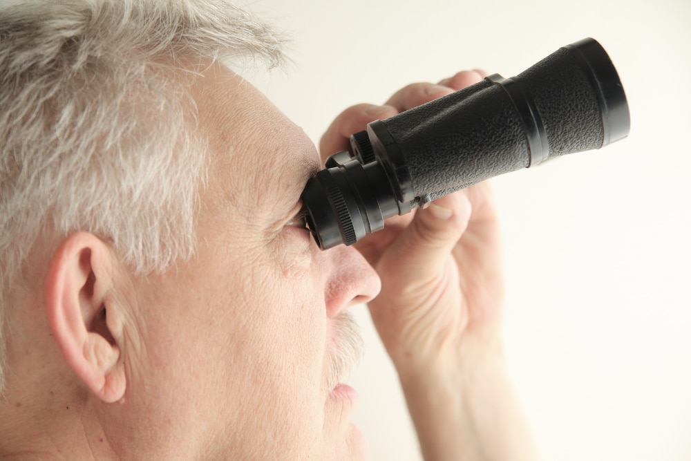 Ein älterer Mann mit einem schwarzen Fernglas, der in die Ferne schaut.