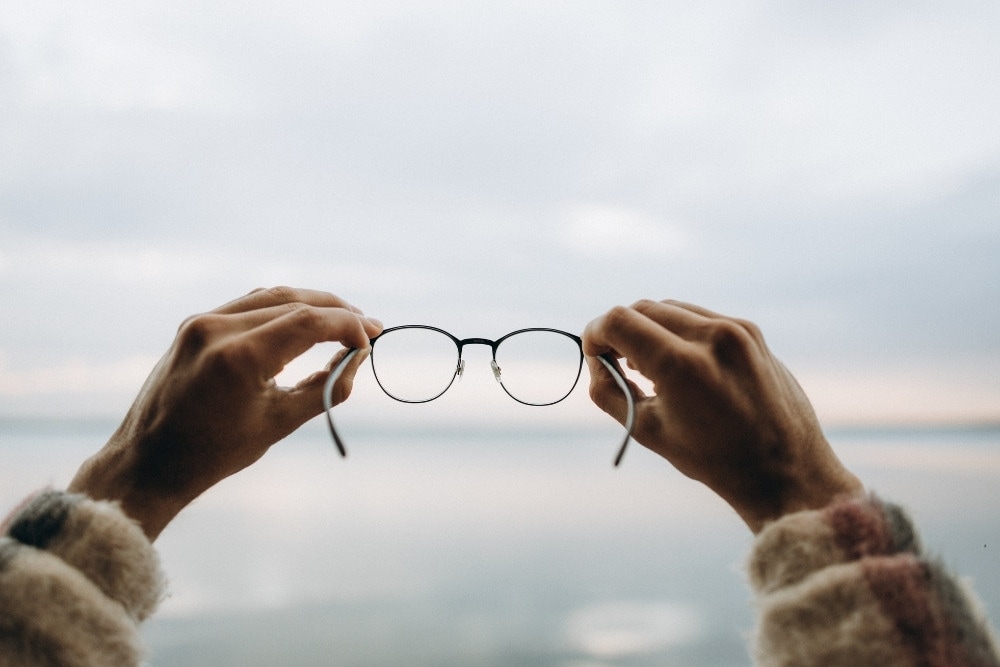 Zwei Hände, die eine Brille in die Höhe halten.